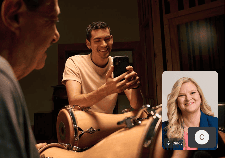 A smiling man sits behind a drum kit while using his smartphone, with an inset video call showing Cindy, a TurboTax representative, illustrating remote tax assistance.