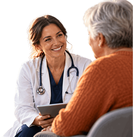 Smiling female physician wearing a white coat and stethoscope holds a tablet while speaking with an older patient in an orange sweater.